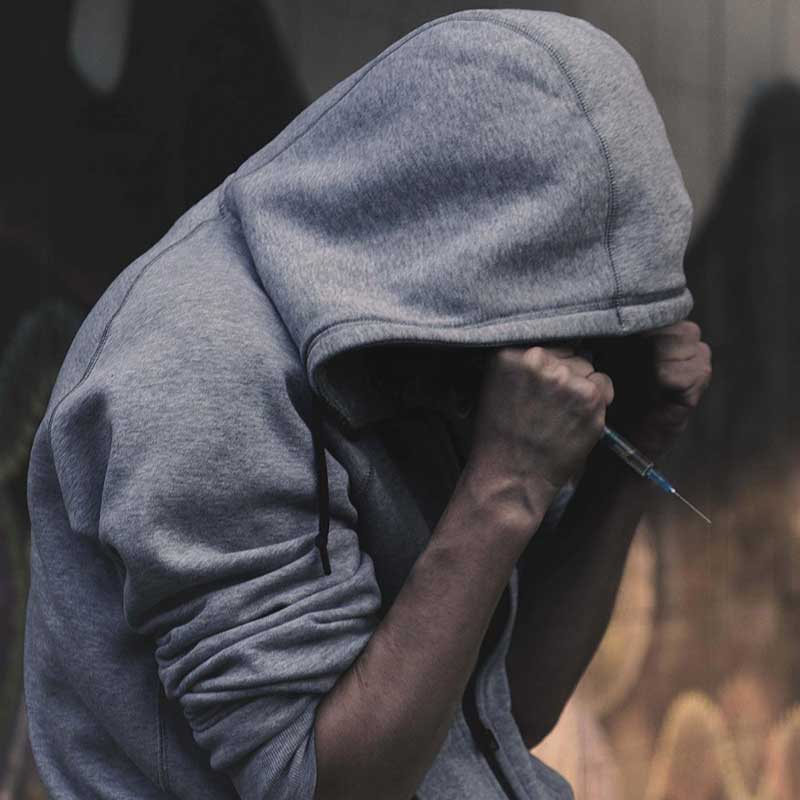 pohled na osobu s kapucí a injekční stříkačkou